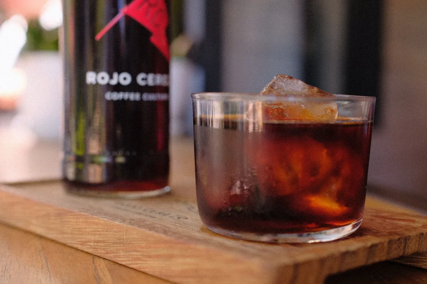 Vaso de cold brew con hielo junto a una botella de Rojo Cerezo