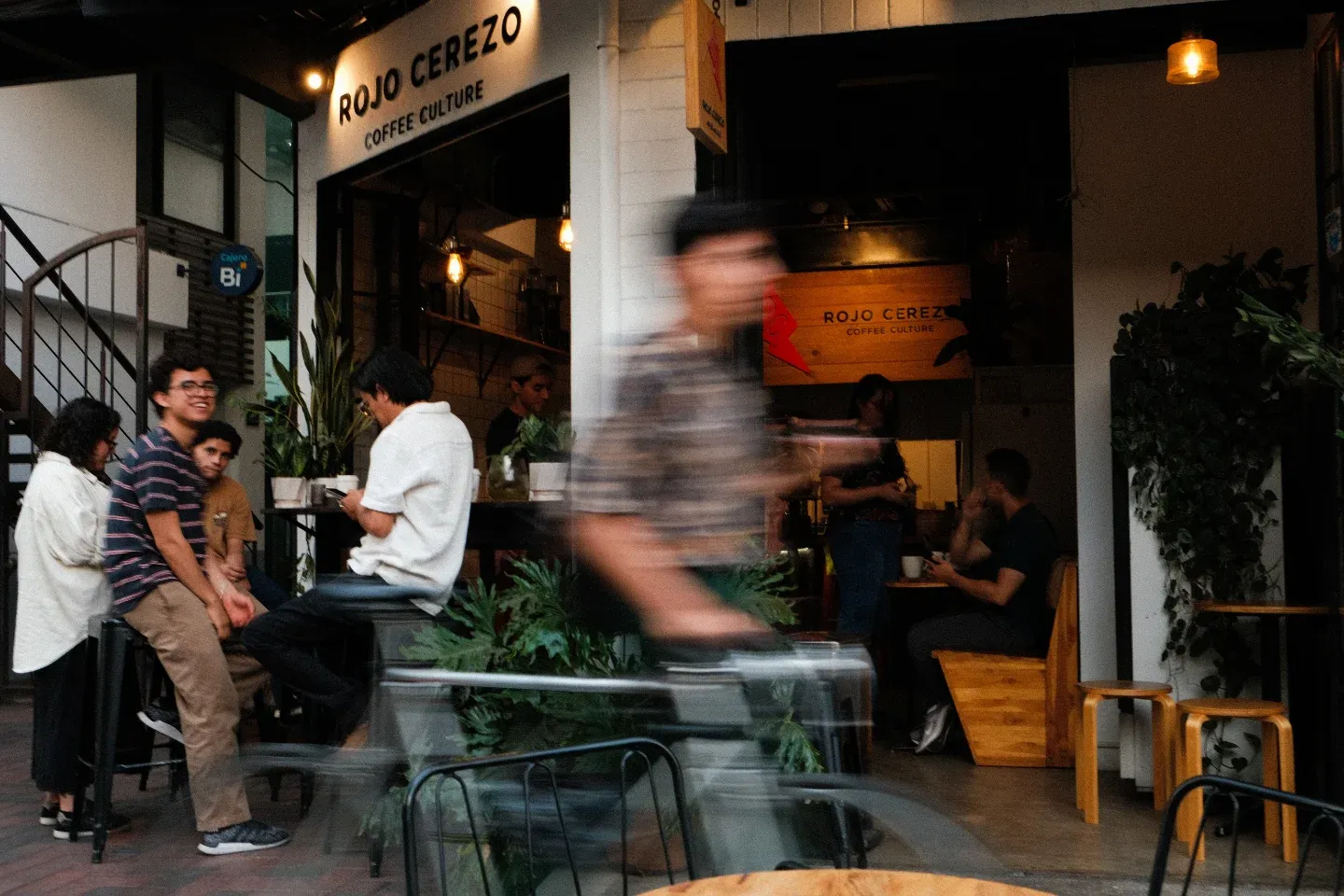 Clientes conversando en las mesas exteriores frente al rótulo de Rojo Cerezo
