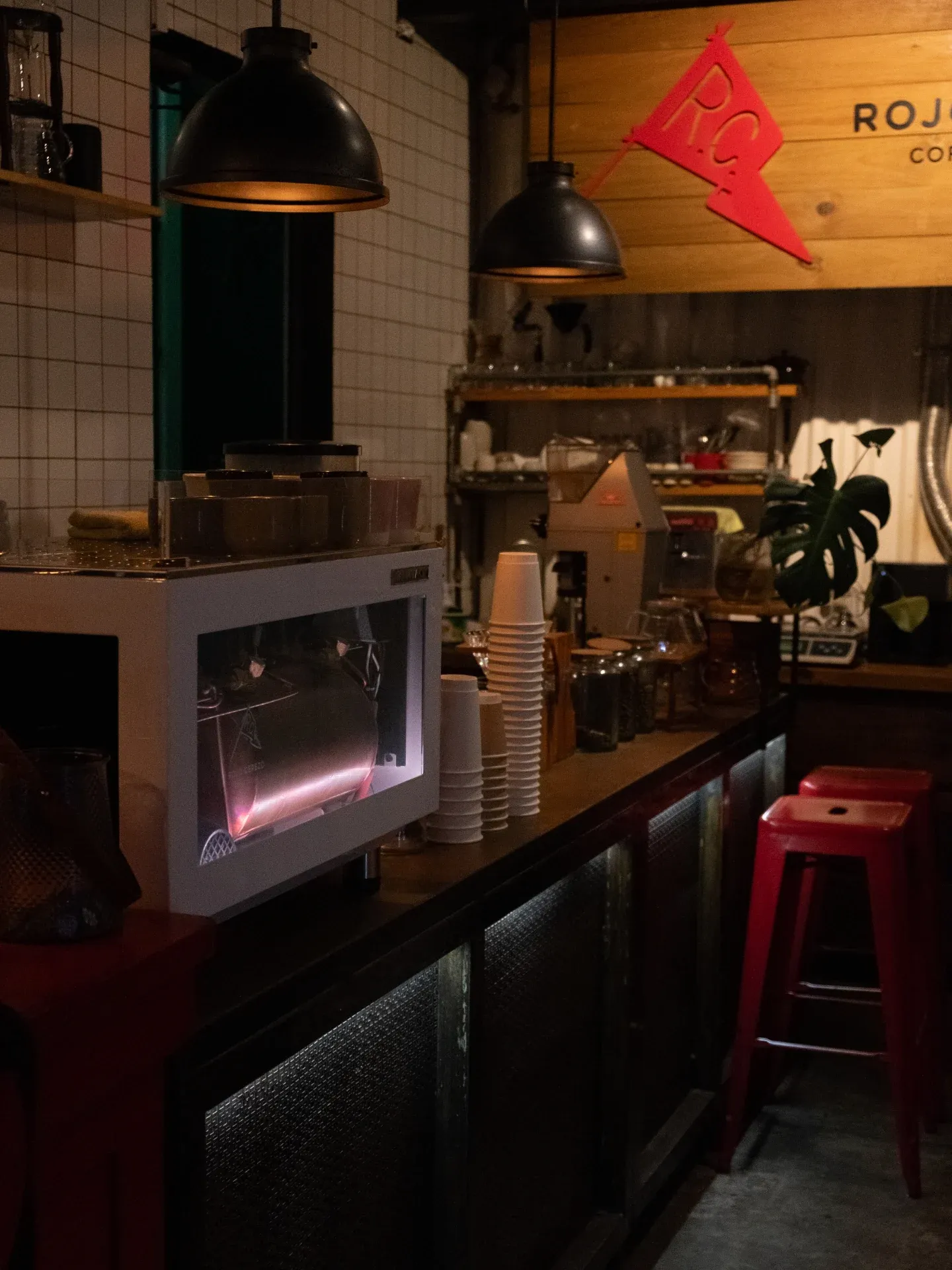 Interior con azulejo blanco, lámparas colgantes y bancos rojos frente a la barra