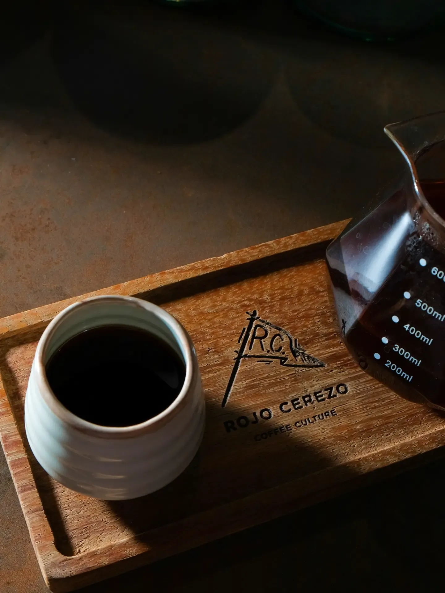 Taza de cerámica sobre una bandeja de madera con el logo de Rojo Cerezo, junto a una jarra de vidrio